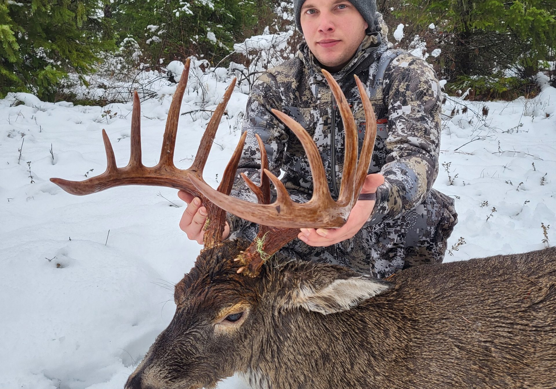 A young man crouches over a downed buck.